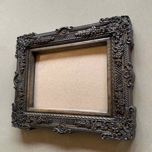 May include: A dark brown wooden picture frame with ornate carvings and a decorative rope design. The frame is empty and ready to display a photo or artwork.