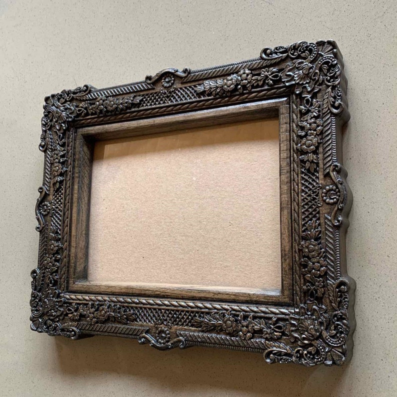 May include: A dark brown wooden picture frame with ornate carvings and a decorative rope design. The frame is empty and ready to display a photo or artwork.
