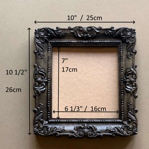 以下が含まれることがあります： 25cm x 17cm の開口部を持つ、濃い茶色の装飾的な絵画フレーム。フレームの高さは 26cm、幅は 16cm です。