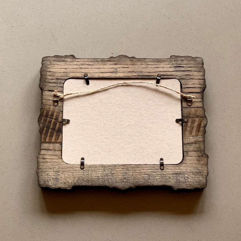 May include: A rustic wooden picture frame with a distressed finish. The frame has a simple design with a rectangular opening and a rope hanger on the back.