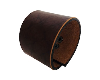 May include: A brown leather cuff bracelet with a dark brown suede lining and three silver rivets.
