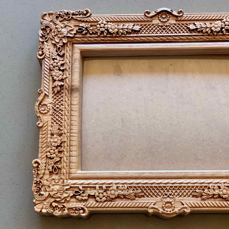 May include: A wooden picture frame with intricate carvings of flowers and leaves. The frame is a light brown color and has a rectangular shape.