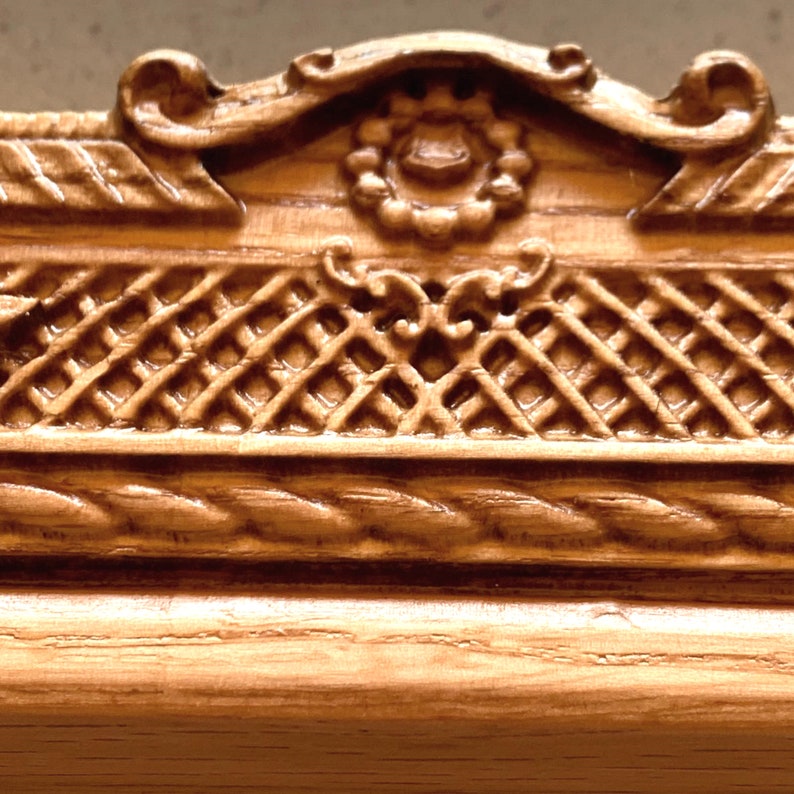 May include: Close-up of a wooden frame with intricate carvings. The frame features a woven pattern, a rope-like design, and a decorative floral motif.
