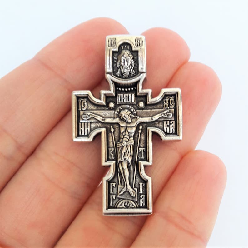 K&ouml;nnte beinhalten: Ein silberner orthodoxer Kreuzanh&auml;nger mit einer Darstellung von Jesus Christus am Kreuz. Das Kreuz ist mit kyrillischen Buchstaben und einem kleinen Bild von Jesu Kopf oben verziert.