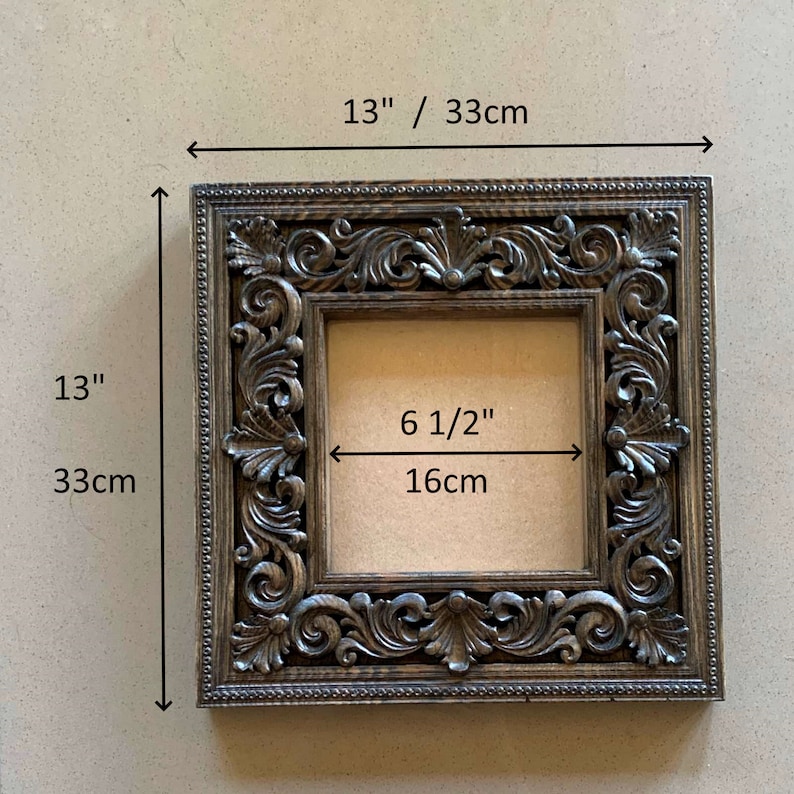 May include: A dark brown wooden picture frame with ornate carvings. The frame measures 13 inches by 13 inches and has an opening of 6 1/2 inches by 6 1/2 inches.