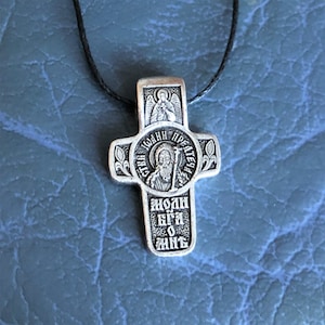 Puede incluir: Un colgante de cruz de plata con una representación de un santo y el texto "Святой Иоанн Предтеча" (San Juan Bautista) y "Моли Бога о нас" (Ruega a Dios por nosotros).