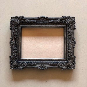 May include: A black ornate picture frame with a detailed design. The frame is empty and ready for a photo or artwork.