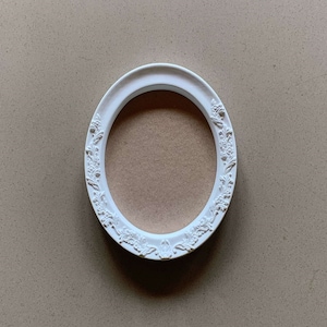 May include: White oval picture frame with an ornate design. The frame is empty and ready for a photo.