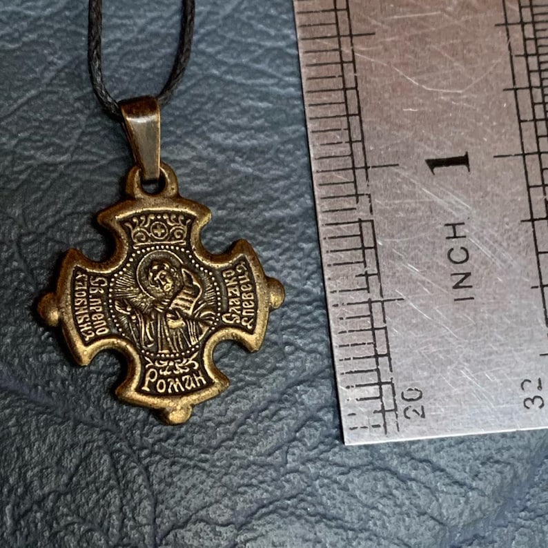 May include: A gold-toned metal pendant with a cross design. The pendant features a depiction of a saint with a crown and the text "St. Gregory the Great" and "Roman" in a circular frame. The pendant is approximately 1 inch in diameter.