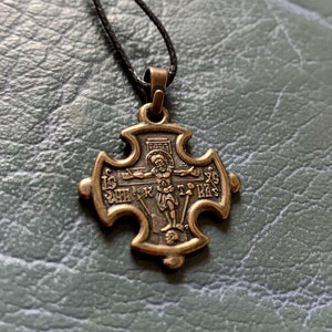 May include: A gold-toned cross pendant with a depiction of Jesus Christ on the cross. The pendant is on a black cord.