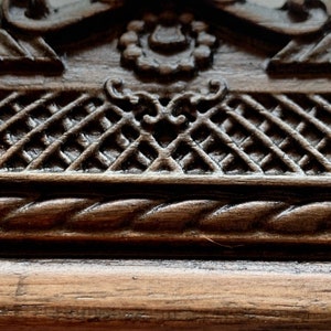 May include: Close-up of a dark brown wooden frame with intricate carvings. The frame features a rope-like design and a decorative pattern of interwoven squares.