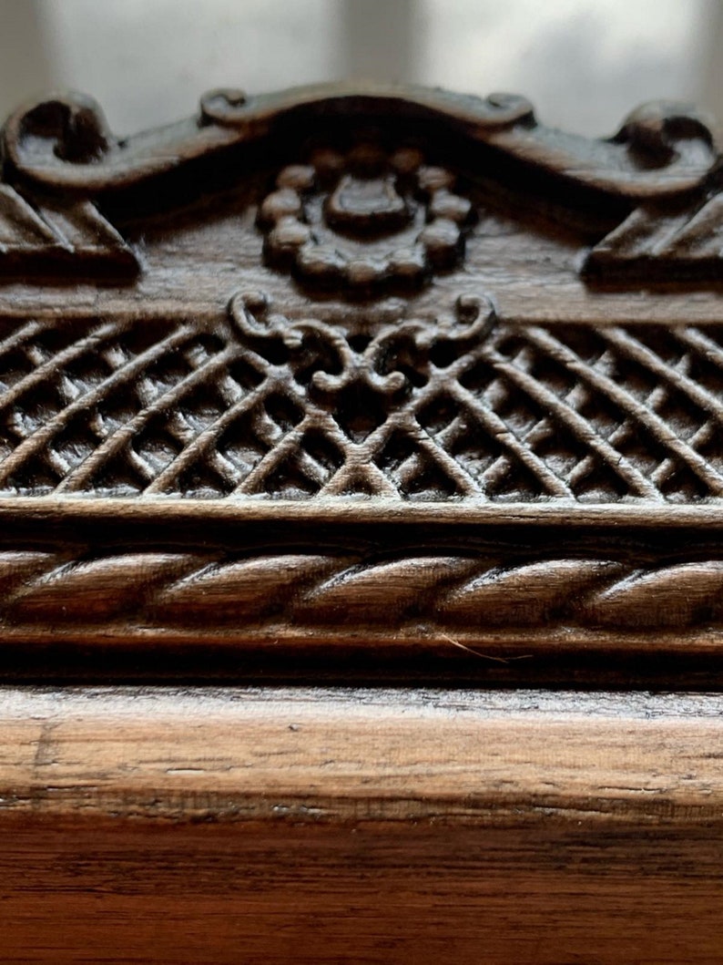 May include: Close-up of a dark brown wooden frame with intricate carvings. The frame features a rope-like design and a decorative pattern of interwoven squares.
