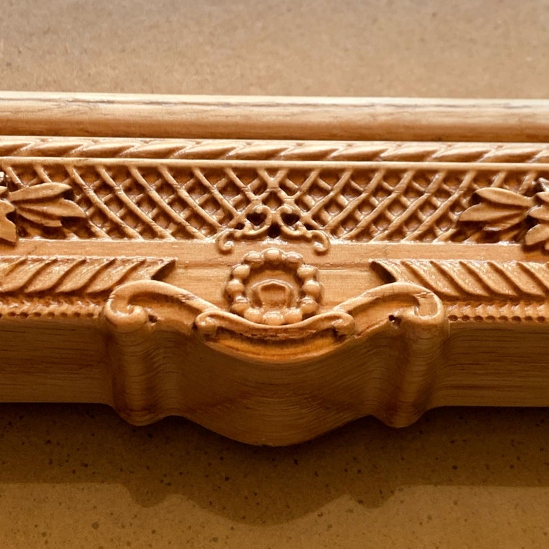 May include: Close-up of a wooden frame with intricate carvings. The frame has a raised, ornate design with a central floral motif.