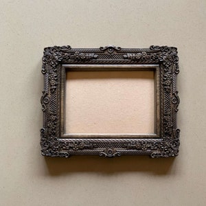 May include: A dark brown ornate picture frame with a decorative, carved design. The frame is empty and ready for a photo or artwork.