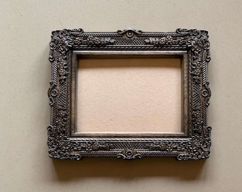 May include: A dark brown ornate picture frame with a decorative, carved design. The frame is empty and ready for a photo or artwork.