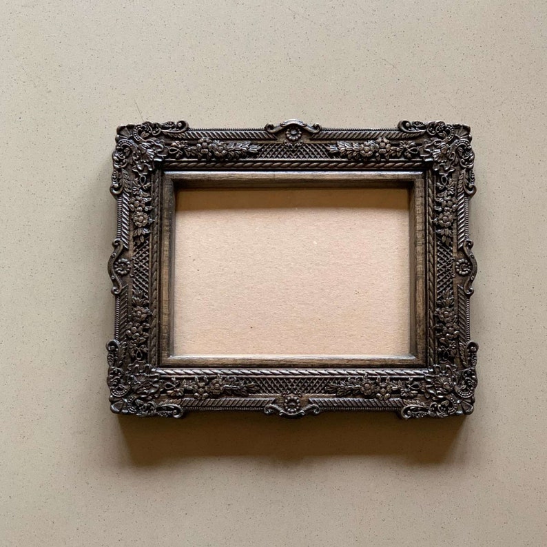 May include: A dark brown ornate picture frame with a decorative, carved design. The frame is empty and ready for a photo or artwork.