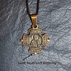 May include: A gold-toned pendant necklace with a cross-shaped charm featuring an image of Saint Anthony. The charm has intricate details and the inscription "Св. ПЕР. АНТОНИН" is visible.