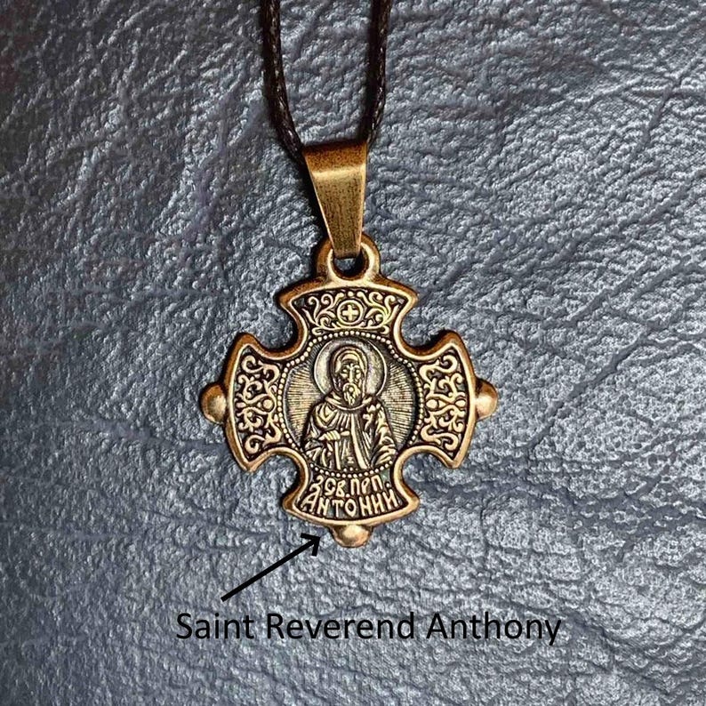 May include: A gold-toned pendant necklace with a cross-shaped charm featuring an image of Saint Anthony. The charm has intricate details and the inscription "Св. ПЕР. АНТОНИН" is visible.