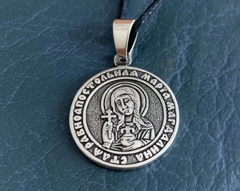 May include: Silver pendant necklace featuring a round icon of Saint Mary Magdalene with a cross and inscription in Cyrillic script: "Святая равноапостольная Мария Магдалина".