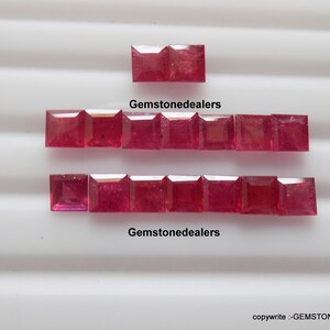 Puede incluir: Una colección de 12 rubíes rojos, dispuestos en dos filas de seis. Las piedras preciosas son de forma cuadrada y tienen un acabado pulido. El texto "Gemstonedealers" aparece dos veces en la superficie blanca.