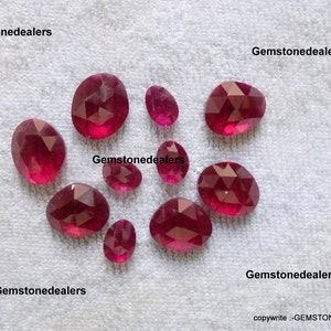 Peut inclure: Une collection de dix pierres précieuses rubis facettées de différentes tailles et formes. Les pierres précieuses sont présentées sur une surface blanche.