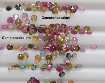 Puede incluir: Una colección de piedras preciosas sueltas facetadas en varios colores, incluyendo rosa, verde y amarillo. Las piedras preciosas están esparcidas sobre una superficie blanca. El texto "Gemstonedealers" aparece dos veces en la imagen.