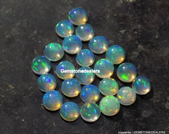 May include: A collection of 20 round, iridescent opal cabochons. The opals are a light blue-green color with flashes of rainbow.