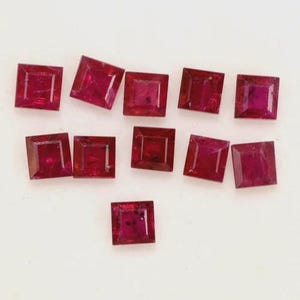 May include: Twelve square-shaped ruby gemstones, each with a deep red colour and a slightly faceted surface.