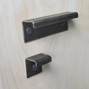 May include: Two black metal drawer pulls, one larger than the other, mounted on a light wood surface.