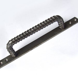 May include: A black metal door handle with a twisted, rebar-style pull. The handle is attached to a flat metal plate with two screw holes.