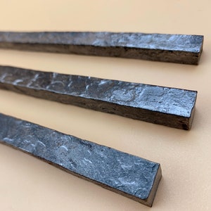 May include: Three long, thin, rectangular pieces of metal with a rough, hammered texture. The metal is a dark grey colour.