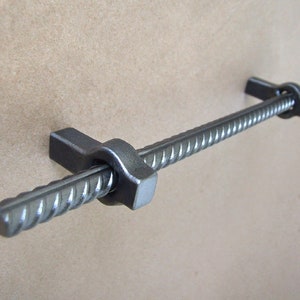May include: A silver metal cabinet pull with a rebar design. The pull has a twisted rebar rod with two metal end caps.
