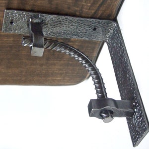 Könnte beinhalten: Eine Metall-Regalhalterung mit gehämmerter Oberfläche. Die Halterung ist mit einer Metallstange und einer Mutter an einem Holzregal befestigt.
