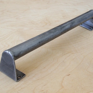 May include: A long, silver-toned metal door pull with squared ends. The pull is made of a thick, round metal bar.