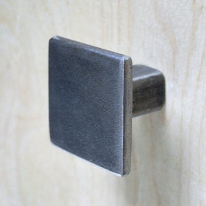 May include: A square-shaped cabinet knob with a brushed metal finish. The knob is made of metal and has a simple, modern design.