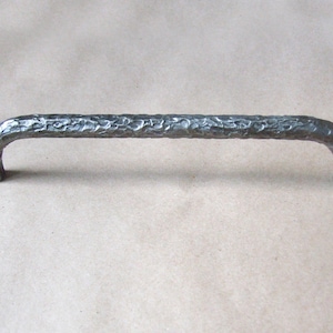 May include: A silver metal cabinet pull with a textured, hammered finish. The pull has a simple, curved design.