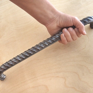 May include: A long, silver, rebar-style door handle with a textured surface. The handle is curved at both ends.