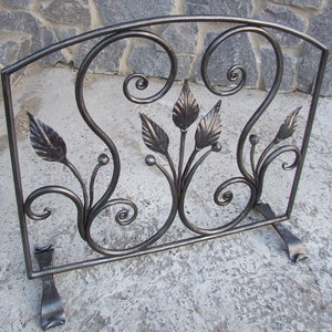 May include: Black metal fireplace screen with a decorative design of stylised leaves and scrolls. The screen has three legs and is freestanding.