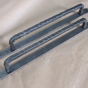 May include: Two long, black metal door handles with a textured, hammered finish. The handles have a simple, rectangular shape with a curved, open top.