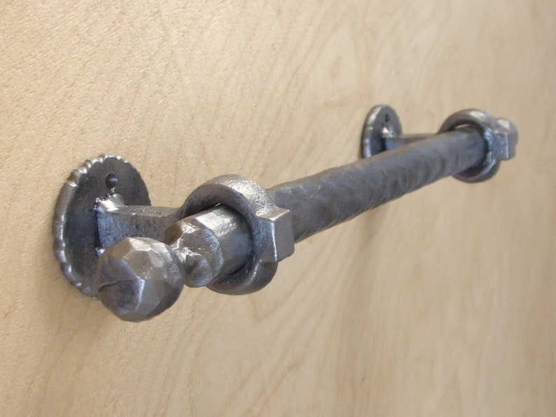 Puede incluir: Un toallero de hierro forjado a mano con acabado martillado y tapas de extremo decorativas. La barra est&aacute; montada en una pared con dos placas redondas de metal.