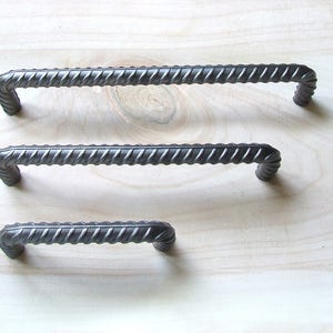 May include: Three black metal drawer pulls with a twisted design. The pulls are different sizes.