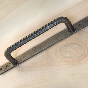 May include: A black metal door handle with a twisted design. The handle is attached to a rectangular metal plate.