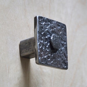 May include: A hammered square metal cabinet knob with a textured surface. The knob is attached to a square metal base.