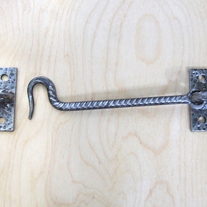 May include: A silver metal door hook with a twisted design. The hook is attached to a square metal plate with two holes. The hook is in the open position.