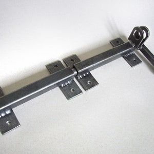 May include: A black metal door latch with a long handle and two rectangular plates. The latch is designed to be mounted on a door or gate.