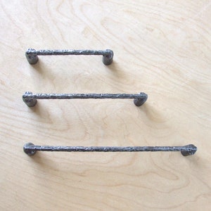 May include: Three black metal drawer pulls with a hammered finish. The pulls are different sizes, with the largest pull at the bottom and the smallest pull at the top.
