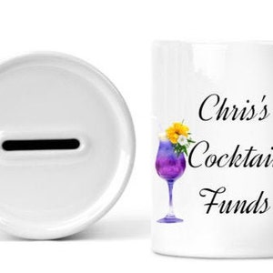 May include: White ceramic piggy bank with a slot on the top. The front of the bank has the text "Chris's Cocktail Funds" with a purple cocktail and a gin and tonic.