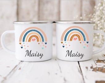 Op de afbeelding: Twee witte emaille mokken met een regenboogontwerp en de naam "Maisy" erop gedrukt. De regenbogen zijn veelkleurig met roze, oranje, geel, bruin, blauw en wit. De mokken hebben zilveren randen.