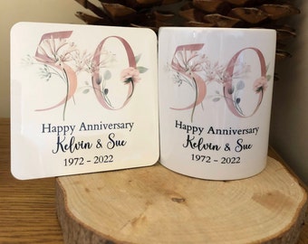 May include: A white ceramic mug and a white coaster with a floral design and the number 50 in pink. The text "Happy Anniversary Kelvin & Sue 1972 - 2022" is printed on both items.
