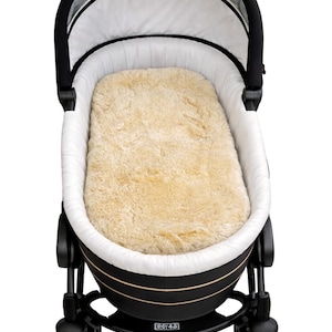 May include: A black and white baby pram with a beige sheepskin-like insert. The pram has a black frame, wheels, and a white interior lining. The canopy is black and white. The pram is designed for infants.